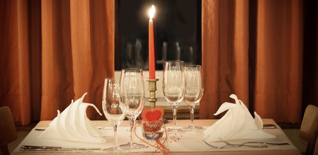 A valentines day dinner table for two with place settings and wine glasses